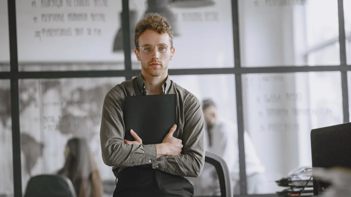 A confident young man standing in a modern office holdin