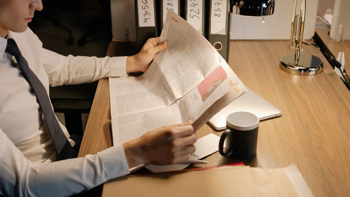 A focused businessman reads a newspaper at a wooden desk