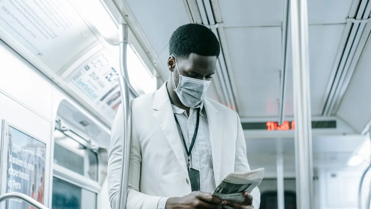 A man in a face mask reads a newspaper on public transpo