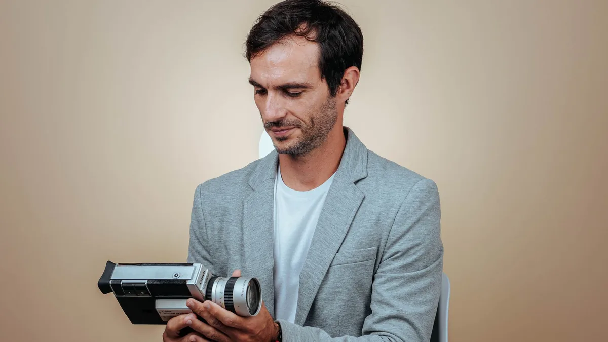 A man in a grey suit examining a vintage camera in a stu