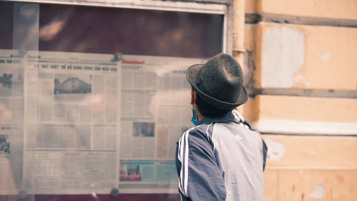 A man in a hat reads a newspaper on an outdoor message b