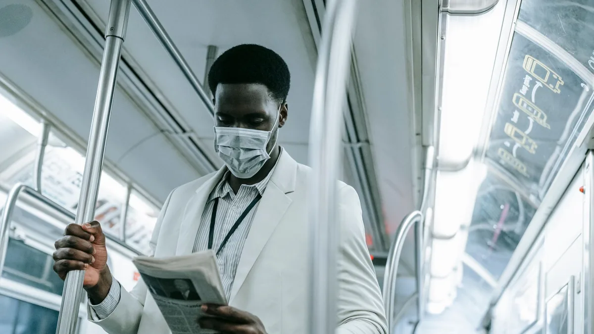 A man in a mask reads a newspaper while standing on a su