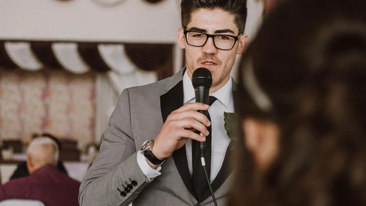 A man in a suit and glasses speaking into a microphone a