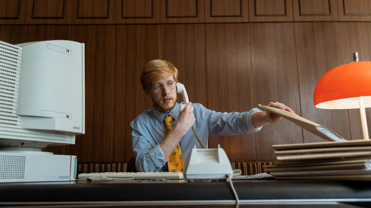 A man in a vintage office setting making a phone call wi