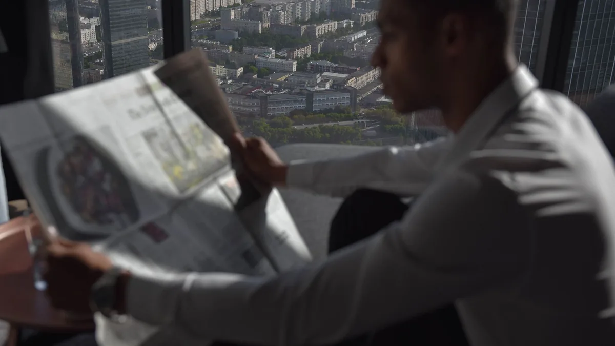 A man in a white shirt reads a newspaper with a high ris