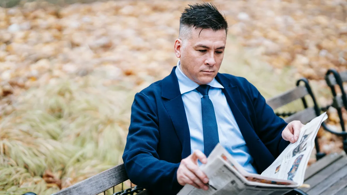 A man in formal attire absorbed in reading a newspaper w