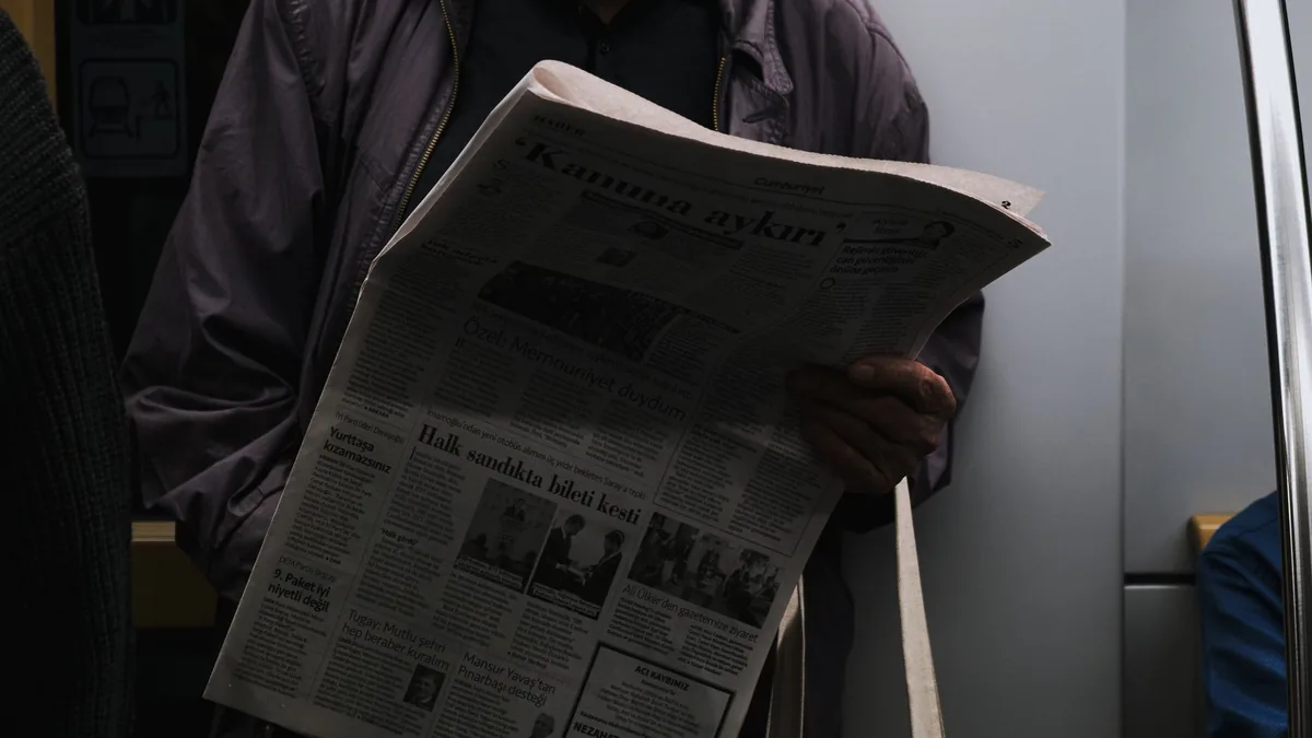 A man reads a newspaper in a dimly lit public transport