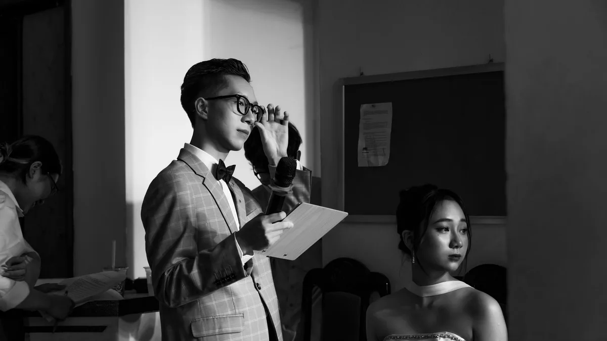 A man speaks into a microphone at an indoor event elegan