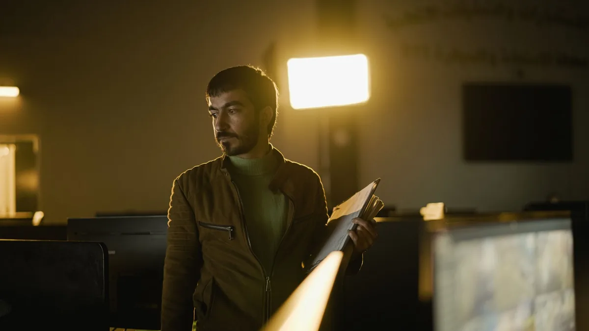 A man stands in a dimly lit office holding files illumin
