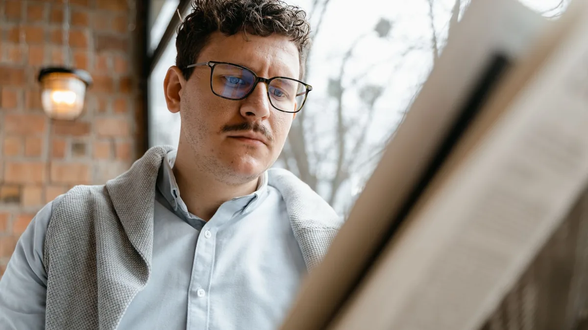 A man with glasses reads a newspaper inside a cozy cafe