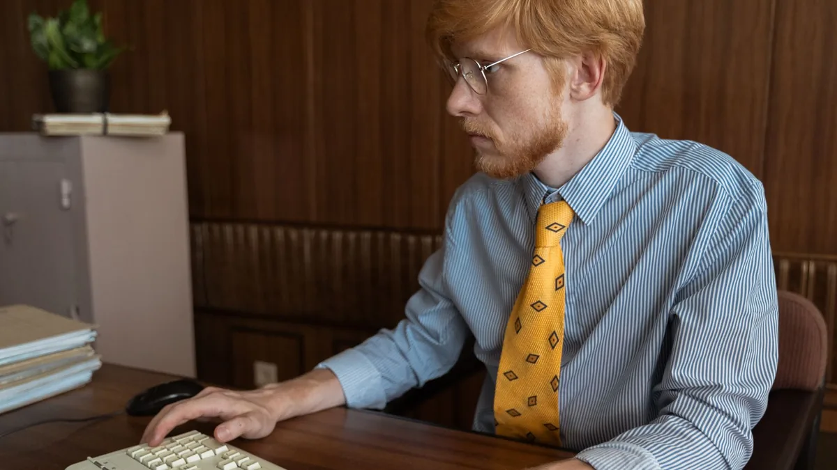 A man with glasses working at a desktop computer in an o