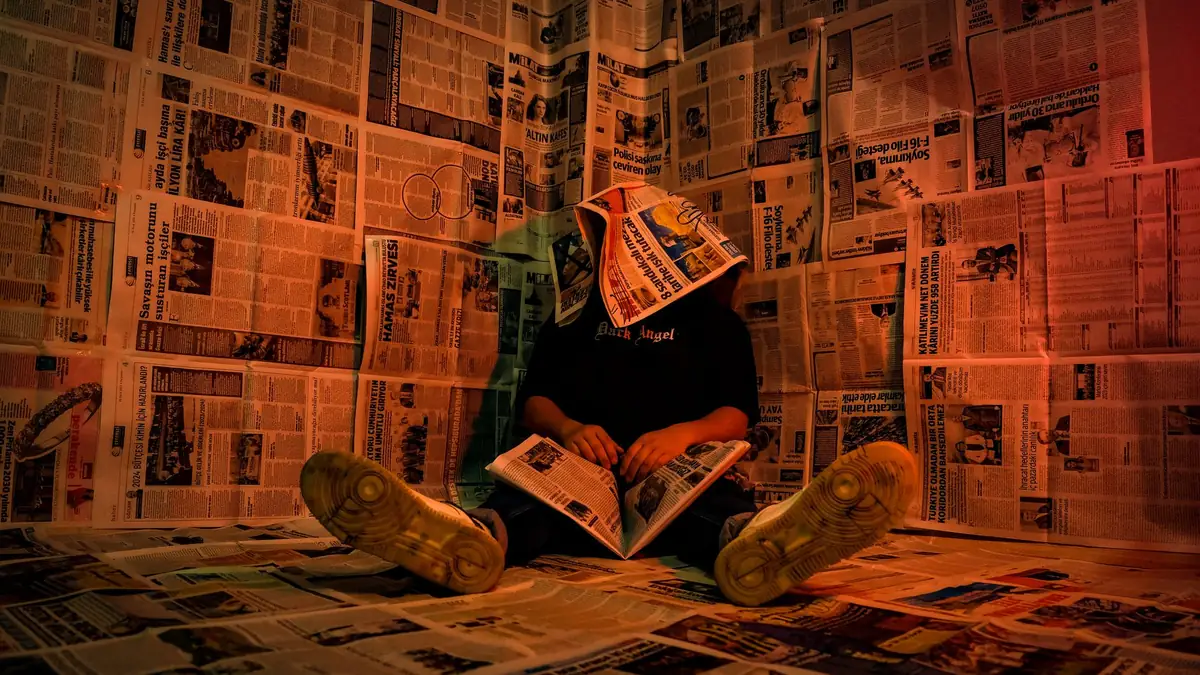 A person sits surrounded by newspapers creating a unique