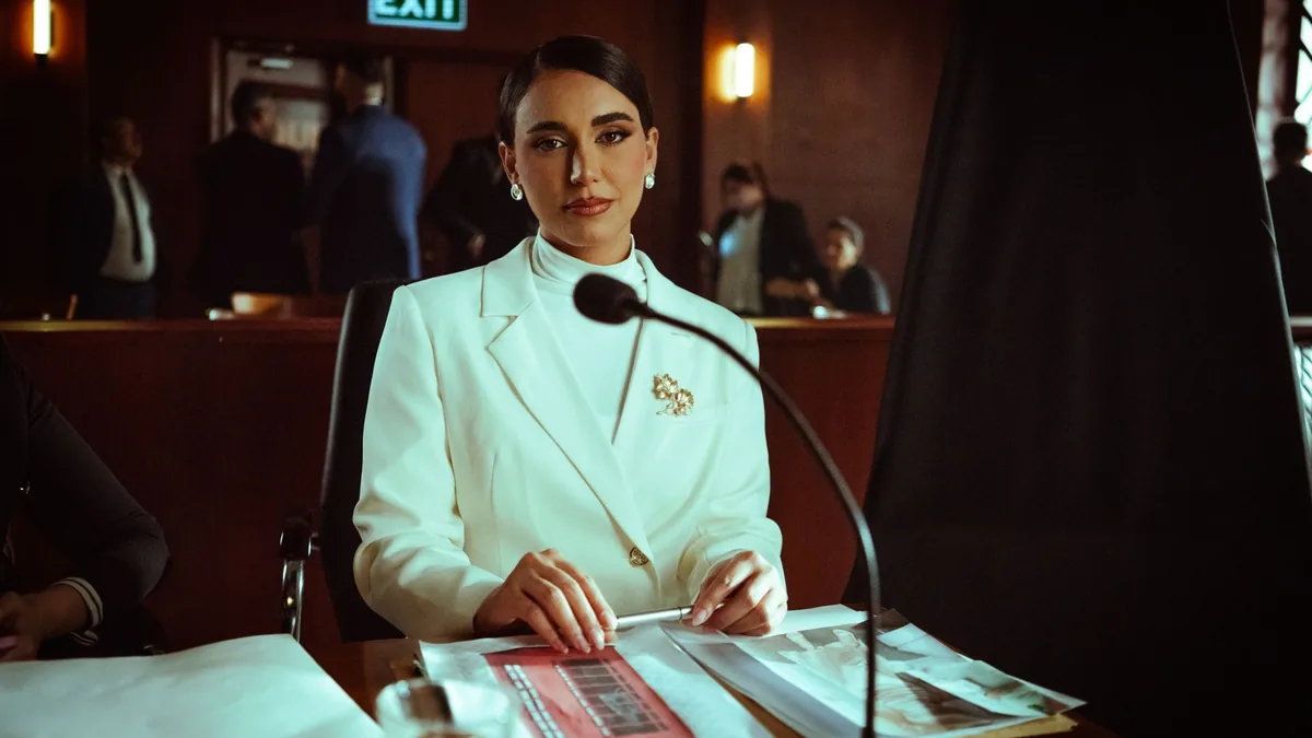 A poised woman in a white suit sits confidently in a cou