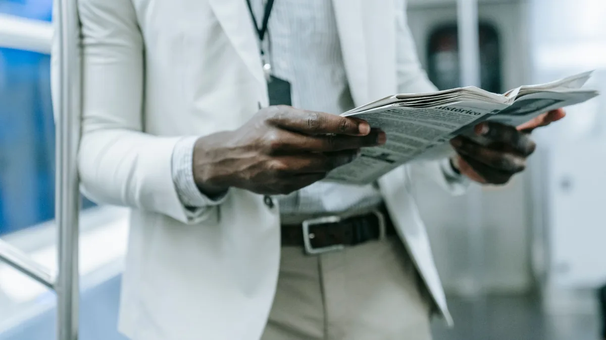 A professional in a blazer reads a newspaper while commu