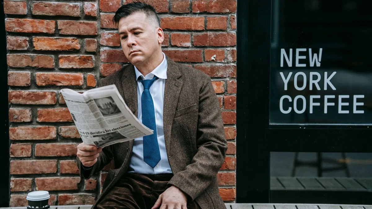 A professional man in formal wear reads a newspaper besi