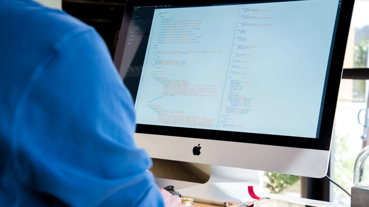 A programmer in a blue shirt coding on an imac perfect f