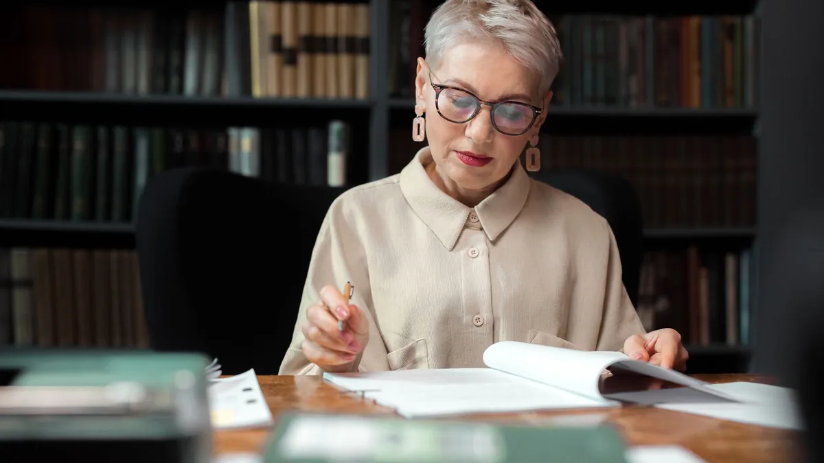 A senior woman wearing eyeglasses and a beige top readin