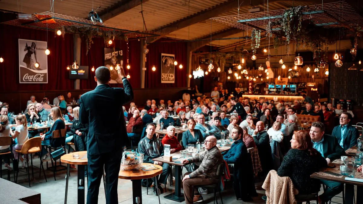 A speaker addressing a large crowd in a vibrant warmly l