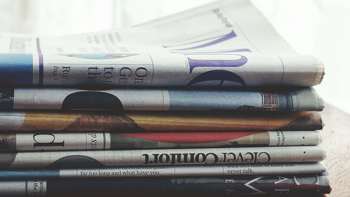 A stack of folded newspapers placed on a wooden table sy