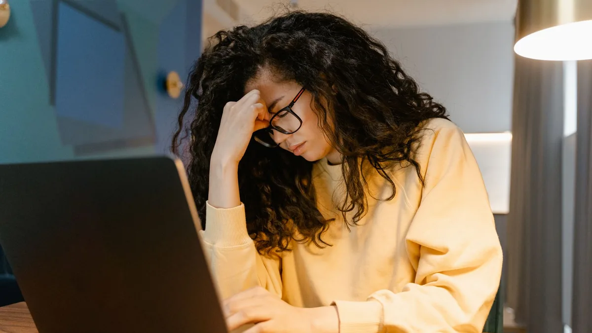 A tired woman with curly hair and glasses experiencing s