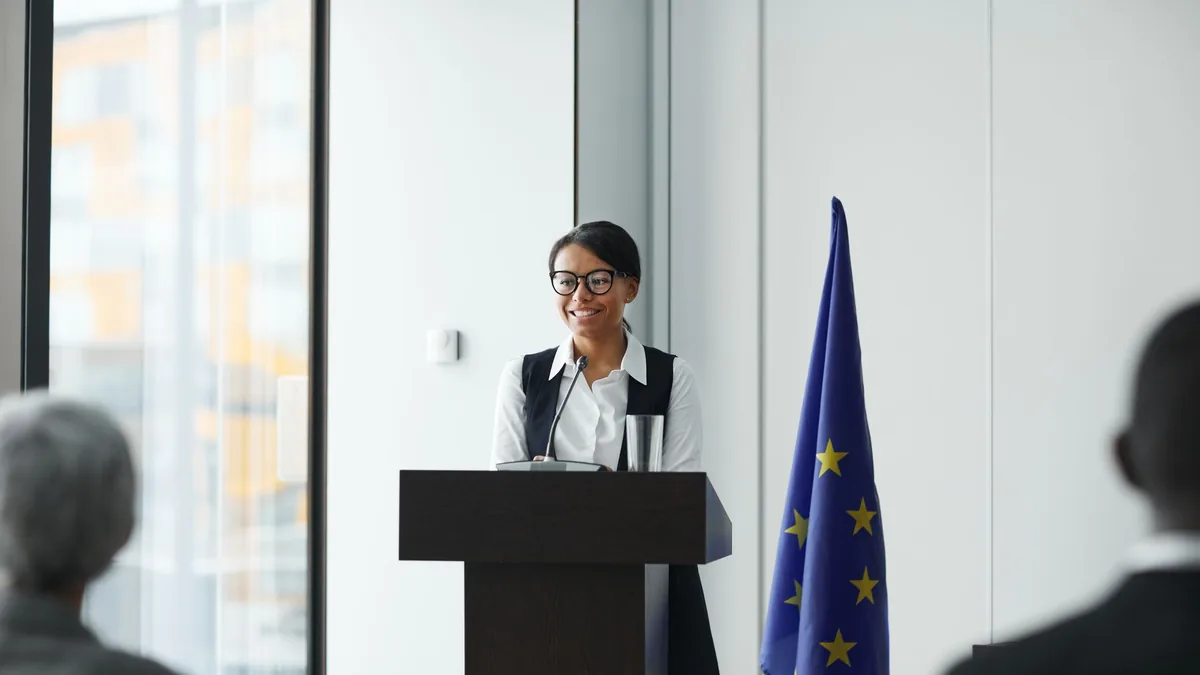 A woman giving a speech at a podium with an eu flag in a