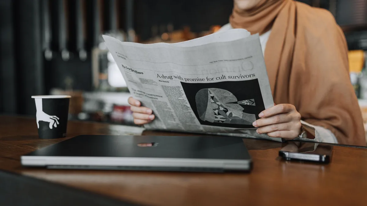 A woman in a caf reading a newspaper with a coffee cup a