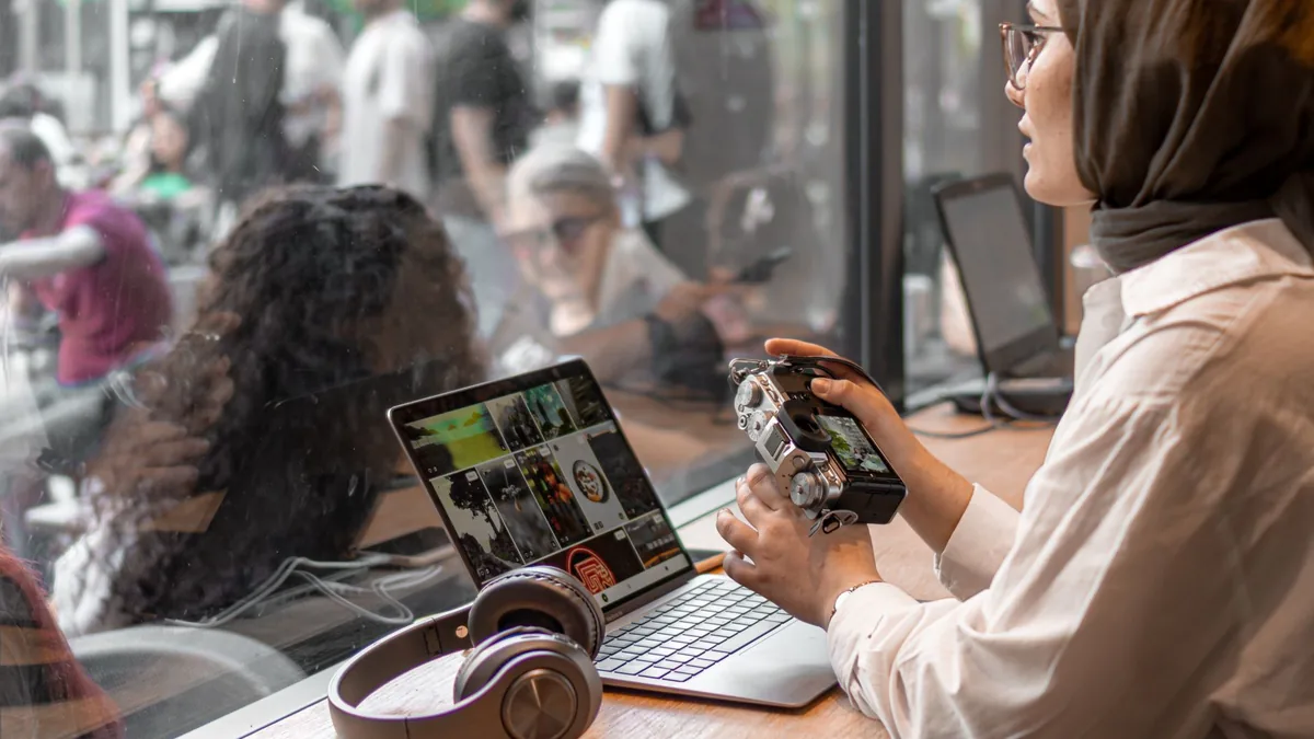 A woman in a hijab using a laptop and camera in a cafe s
