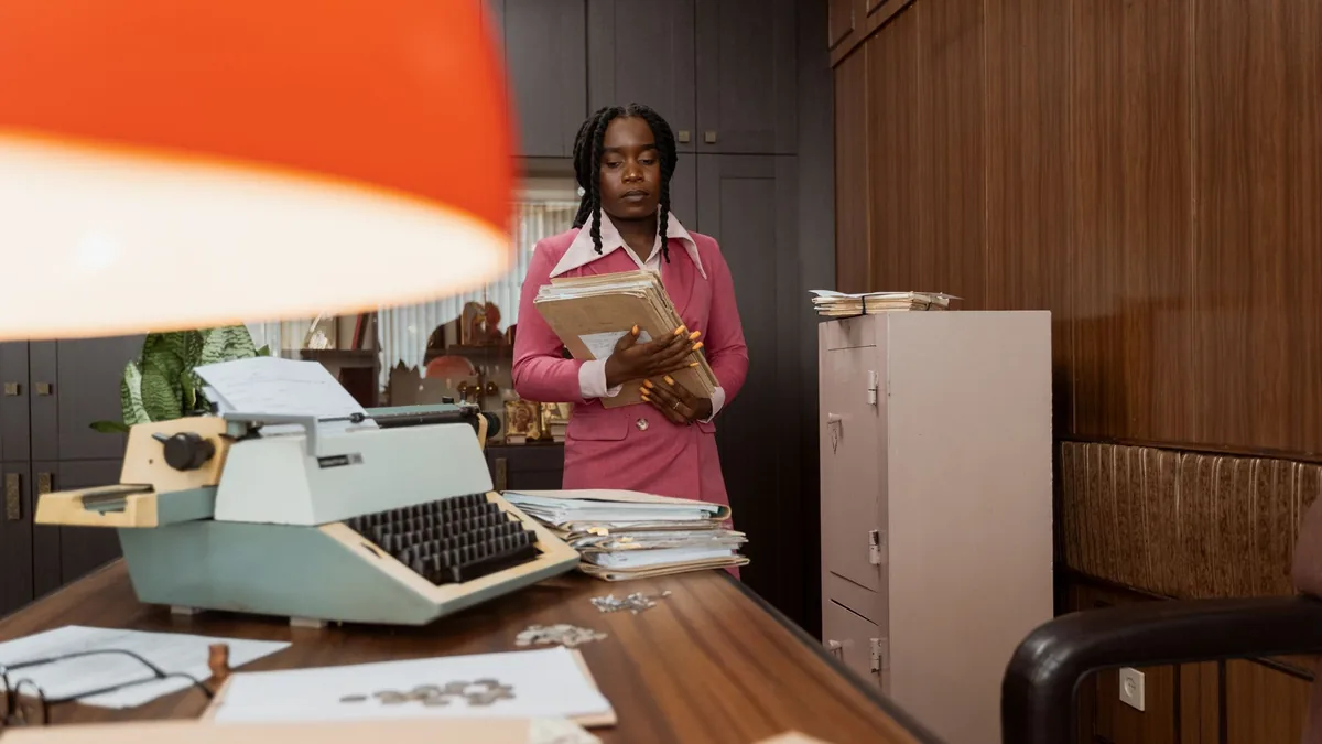 A woman in a pink outfit holds files in a vintage office