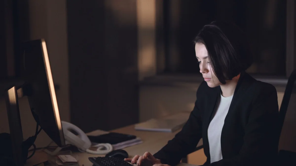 A woman in a suit works late at a dimly lit office desk