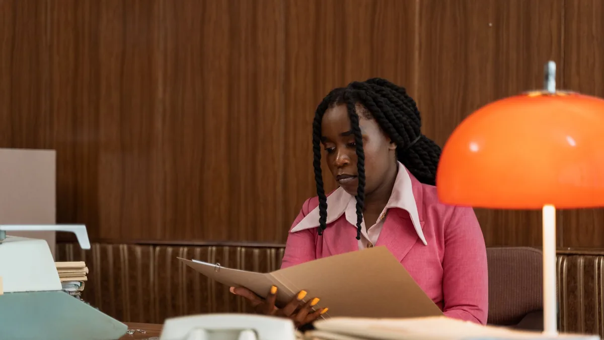 A woman in a vintage office setting reading a folder sur