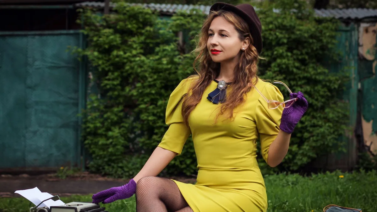 A woman in a vintage outfit sits outdoors with a typewri