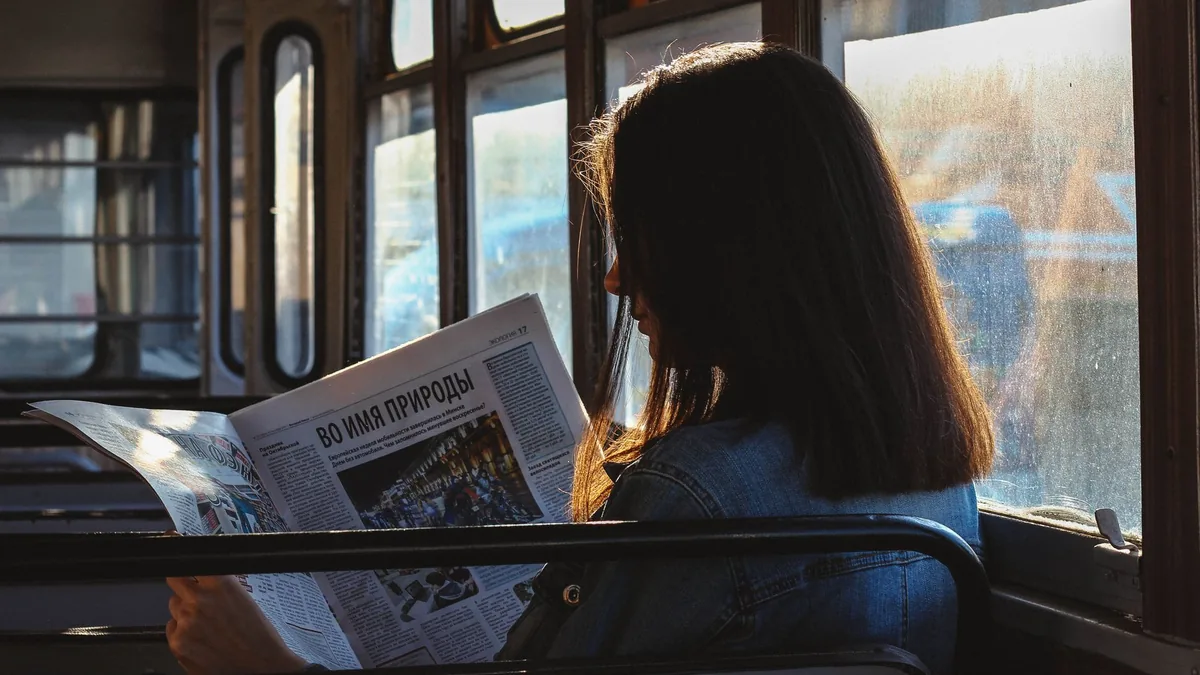 A woman reads a newspaper in a sunlit bus capturing a mo
