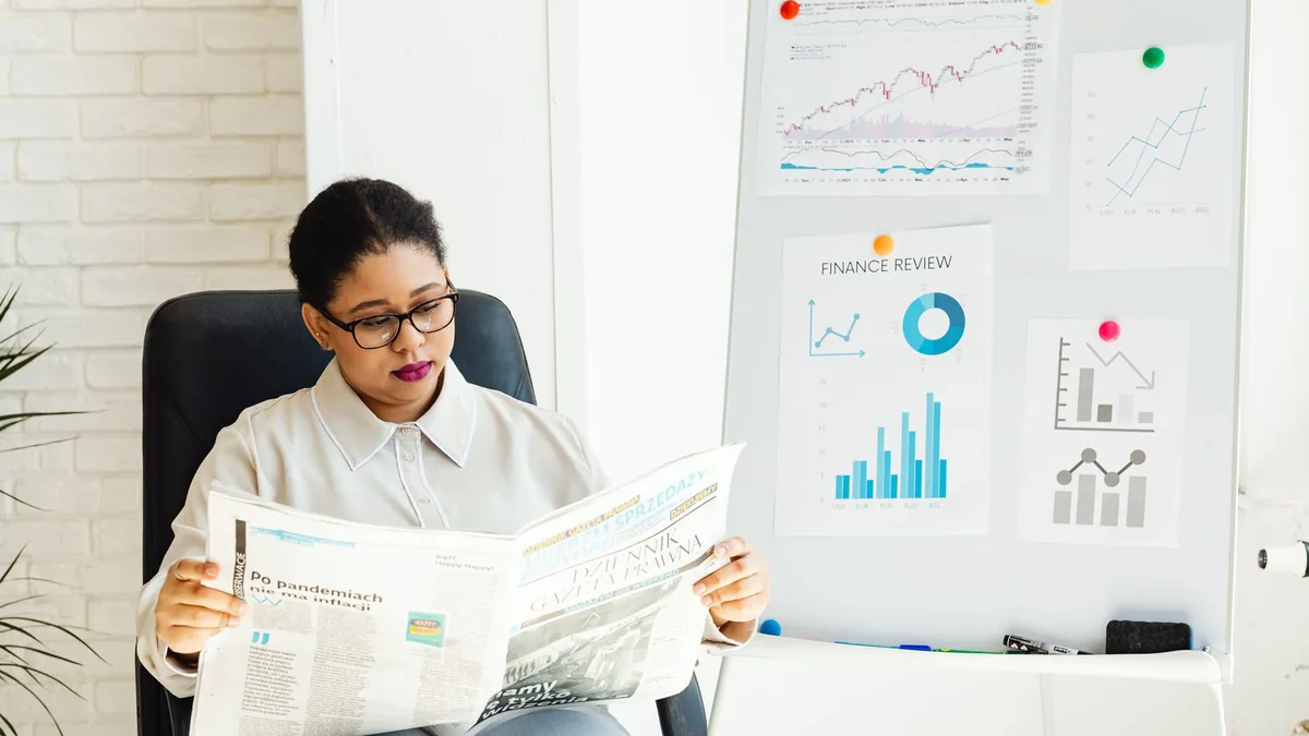 A woman reads a newspaper with stock charts displayed in