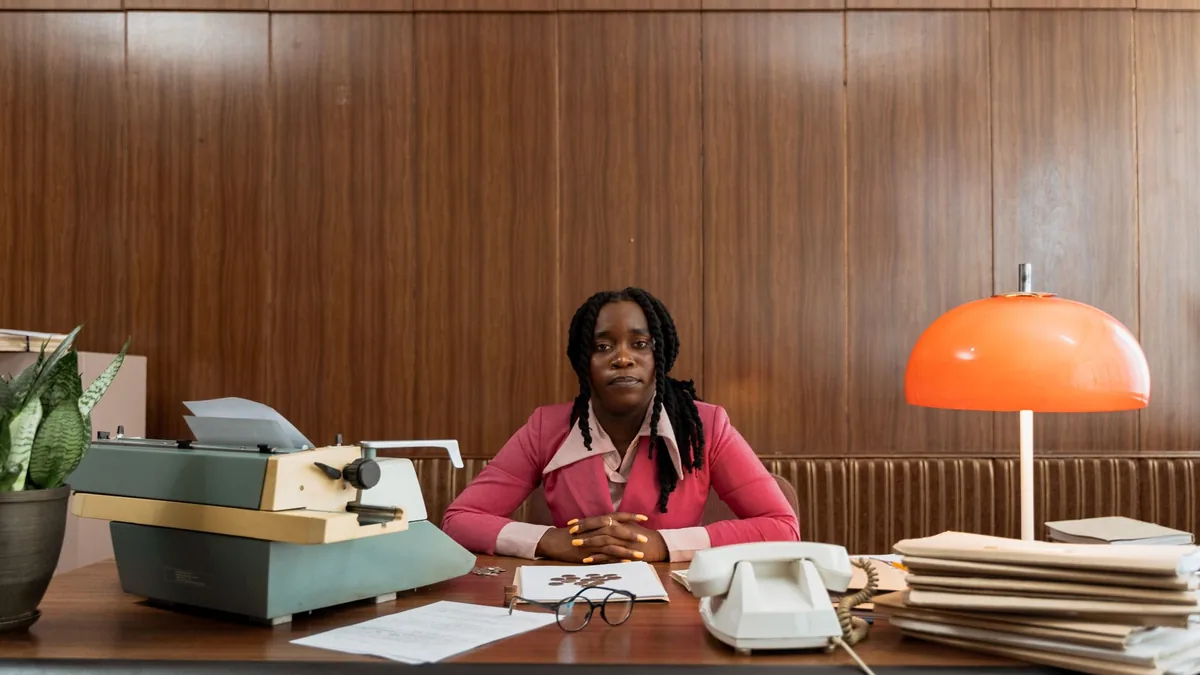 A woman sits at a vintage office desk with a typewriter