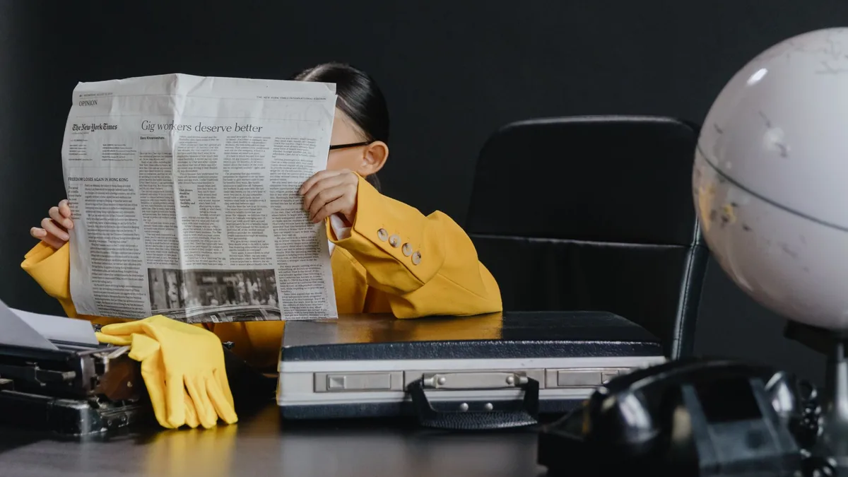 A young girl in a yellow suit reading a newspaper at a d