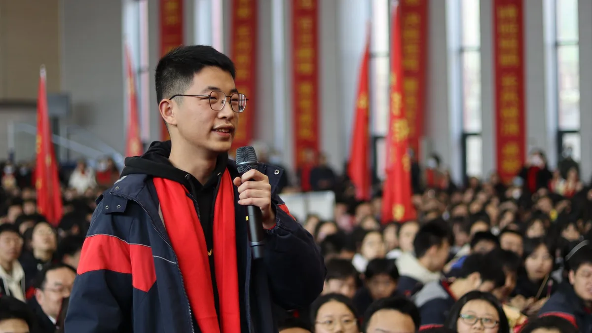 A young man speaking at a crowded indoor event symbolizi