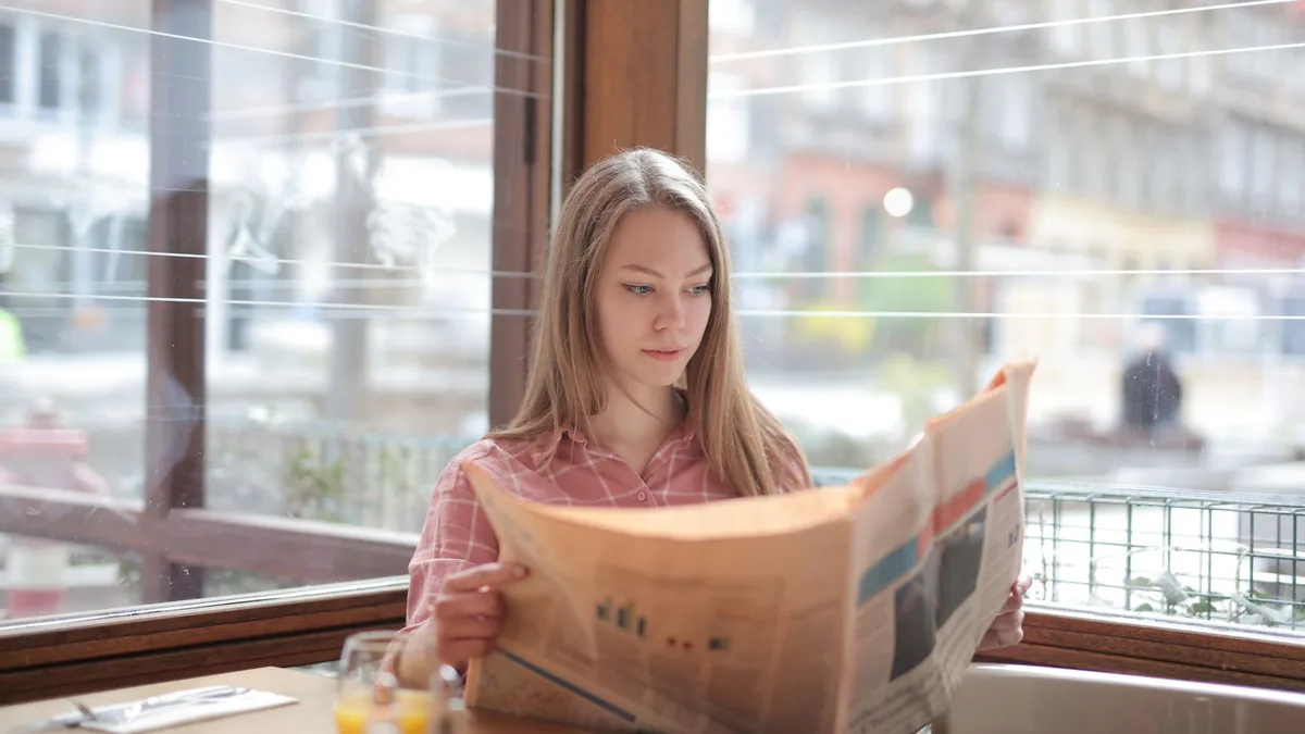 A young woman enjoying a newspaper at a cafe table immer
