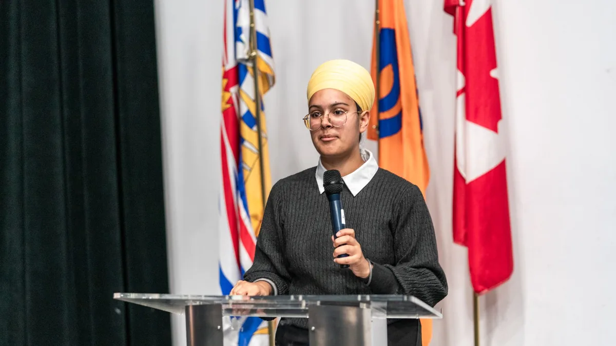 A young woman wearing a turban speaks at a podium with i