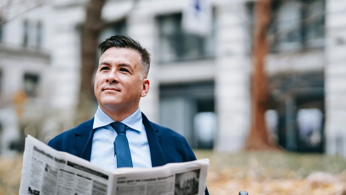 Adult man in suit reading newspaper outdoors on a bench