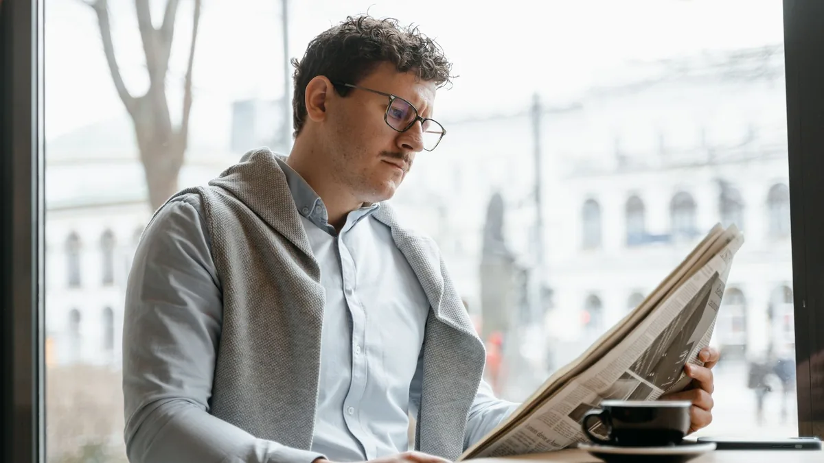 Adult man reads a newspaper by a caf window enjoying a c