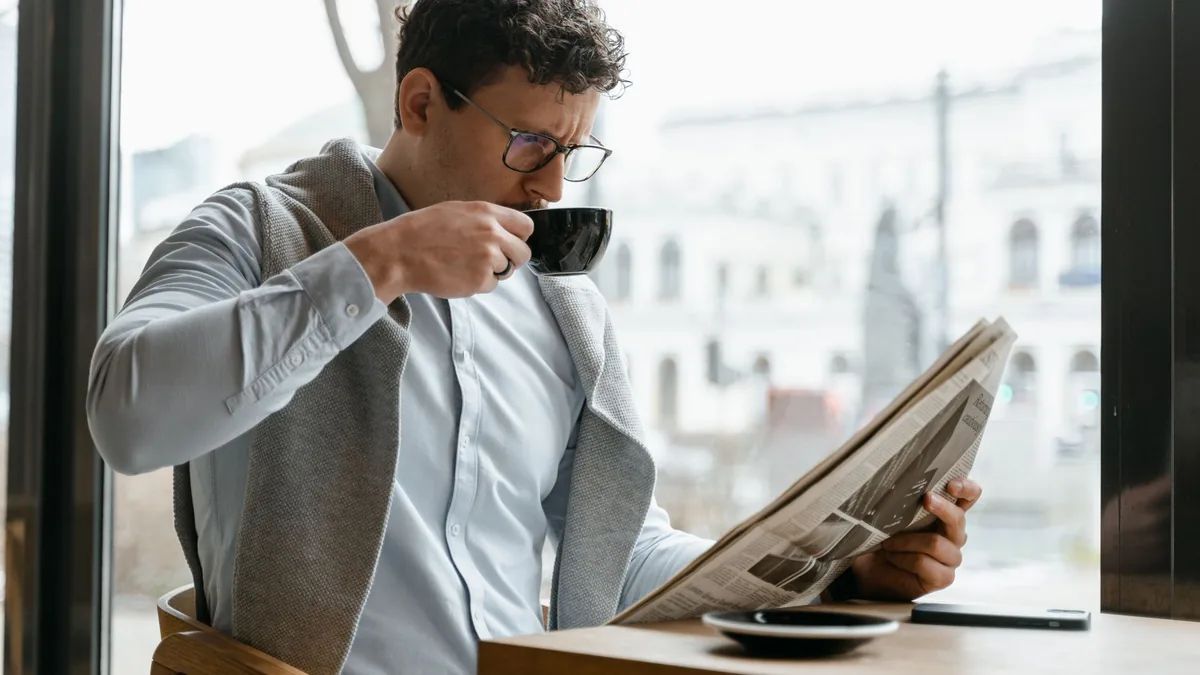Adult man wearing eyeglasses sipping coffee and reading