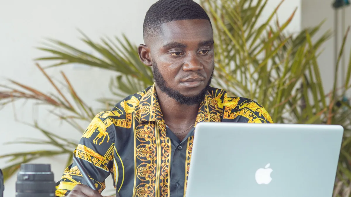 African man using a laptop outdoors with camera equipmen