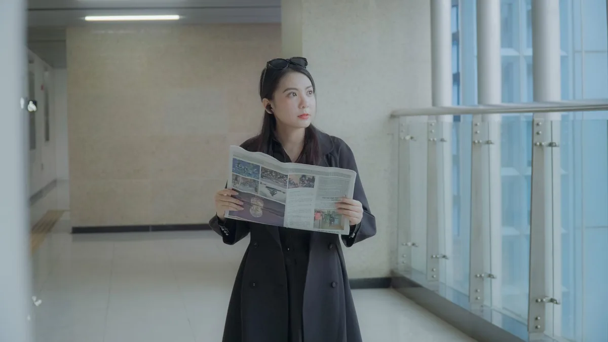 An adult woman in a coat reads a newspaper in a modern i