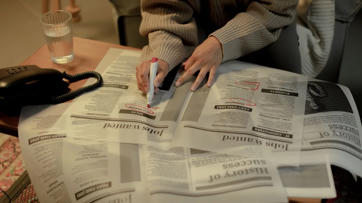 An adult woman marks job listings in a newspaper while s