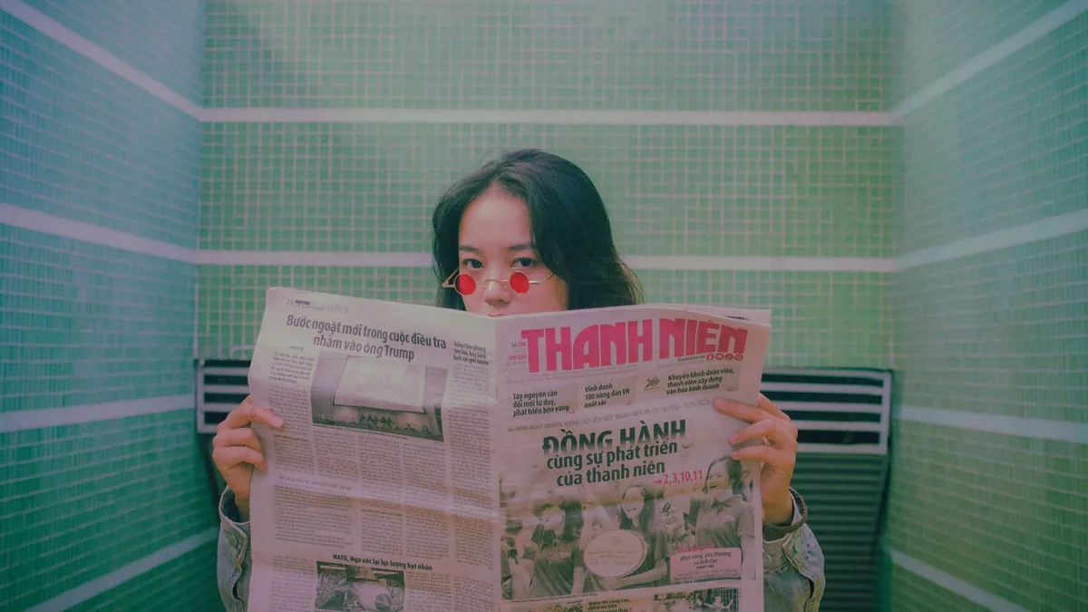 An asian woman wearing sunglasses reading a newspaper wi