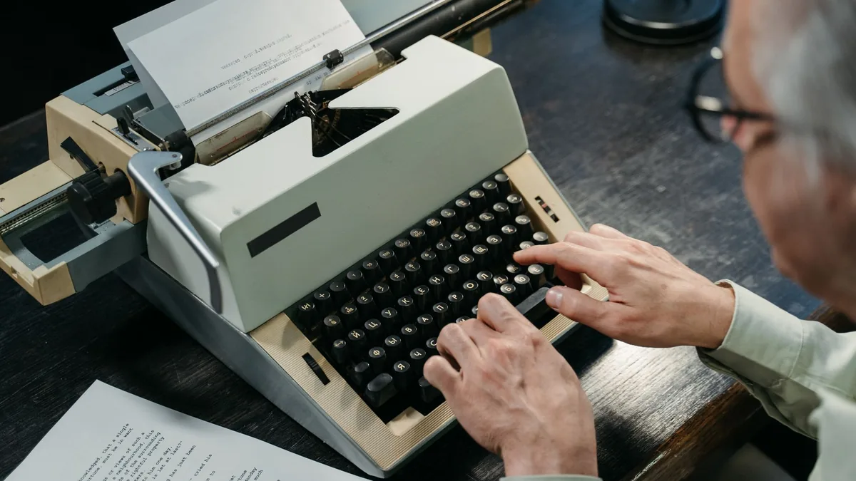 An elderly person types on a vintage typewriter capturin