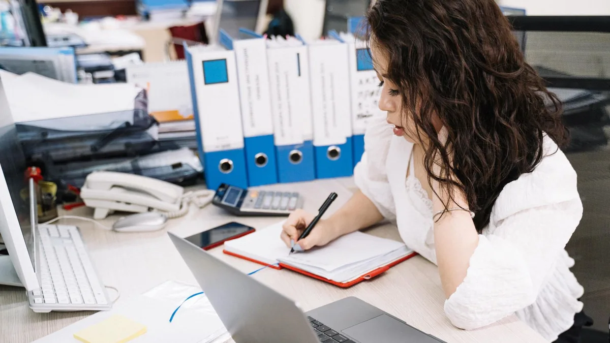 An office worker takes notes while working at a desk wit