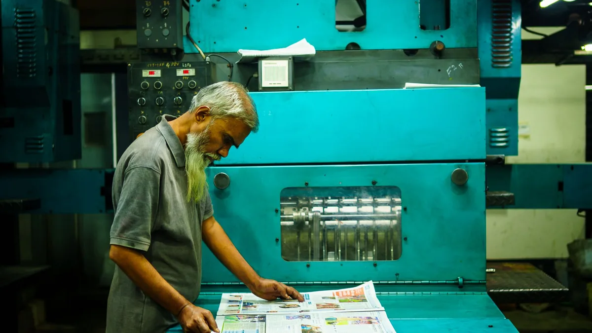 An older man examines freshly printed materials at a lar