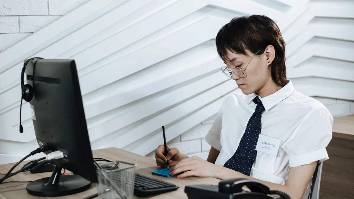 Asian call center agent writing notes at a modern desk s