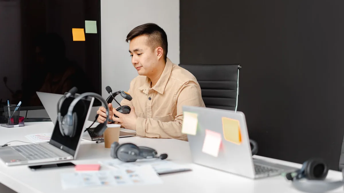 Asian man in an office setting using a laptop and headse